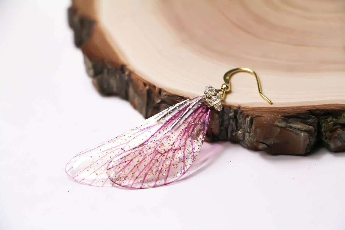 Magico paio di orecchini composto da due ali di fata in delicato rosa cipria, impreziosite da una leggera spolverata di glitter iridescenti.