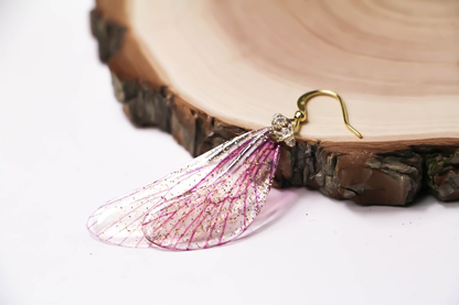 Magico paio di orecchini composto da due ali di fata in delicato rosa cipria, impreziosite da una leggera spolverata di glitter iridescenti.